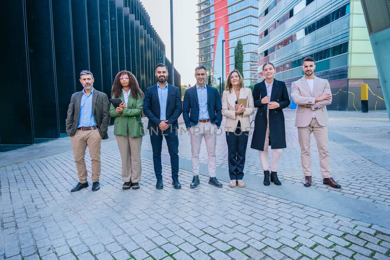 A diverse group of business professionals standing confidently outdoors in a modern cityscape. They are dressed in formal and smart casual attire, representing teamwork and success.
