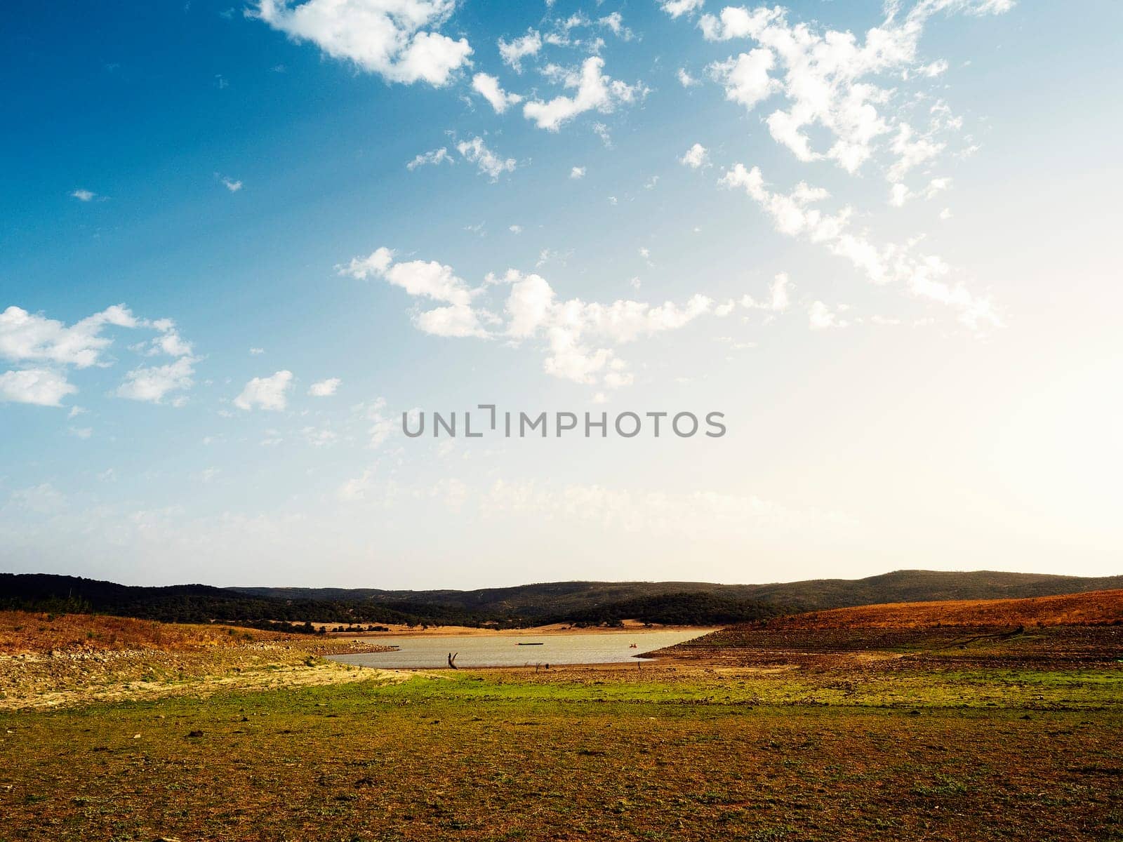 large open field with a lake in the middle, the sky is clear and blue with few clouds scattered, concept of peaceful and serene landscape in the vast expanse of land, copyspace for text