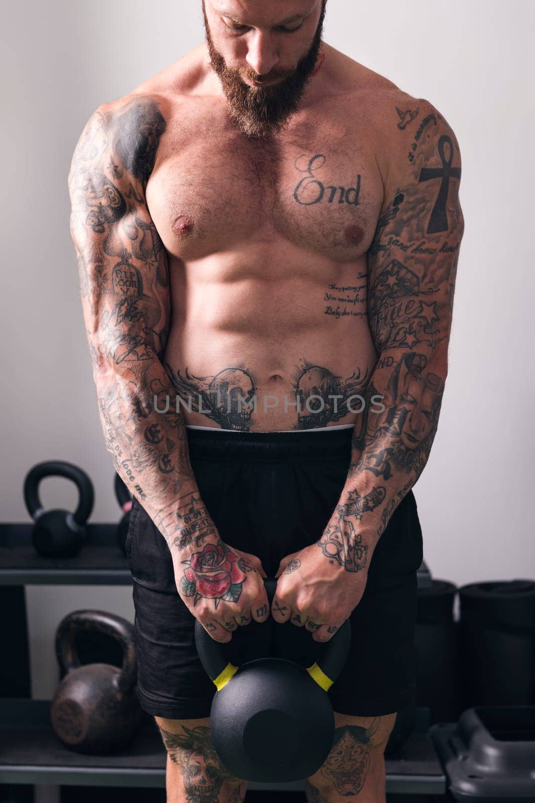powerful shirtless bodybuilder with tattoos doing exercise with heavy kettlebell during functional training in gym, concept of fitness and active lifestyle