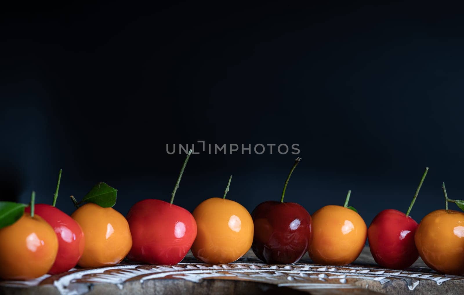 View of Deletable imitation fruits (Kanom look choup) in the shape of fruits has a sweet taste on wooden cutting board. Traditional thai sweet treats made from mung beans and coconut milk, and glazed in shiny agar agar jelly, Auspicious thai dessert, use it as your Wallpaper, Poster and Space for text, Selective focus.