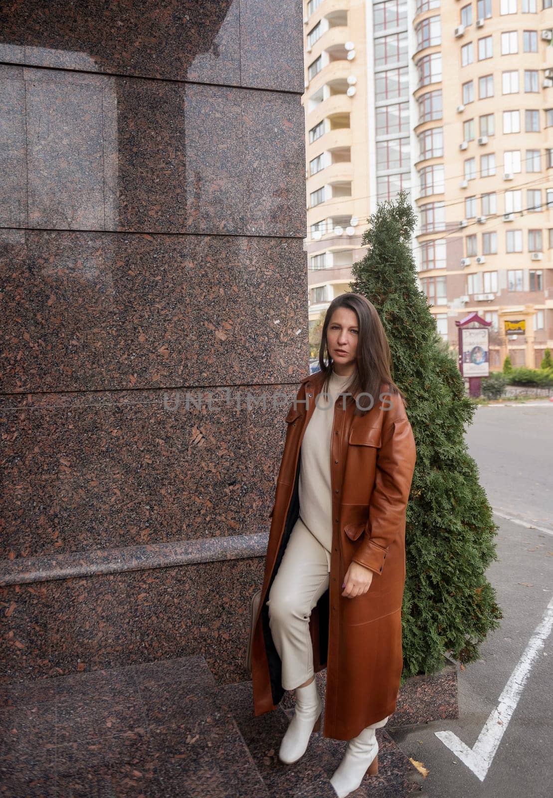 elegant woman over 40 exiting building with laptop bag. She is wearing a brown coat, holding a laptop bag. She is elegant in white shoes. She is a slim, well-groomed woman working in an office.
