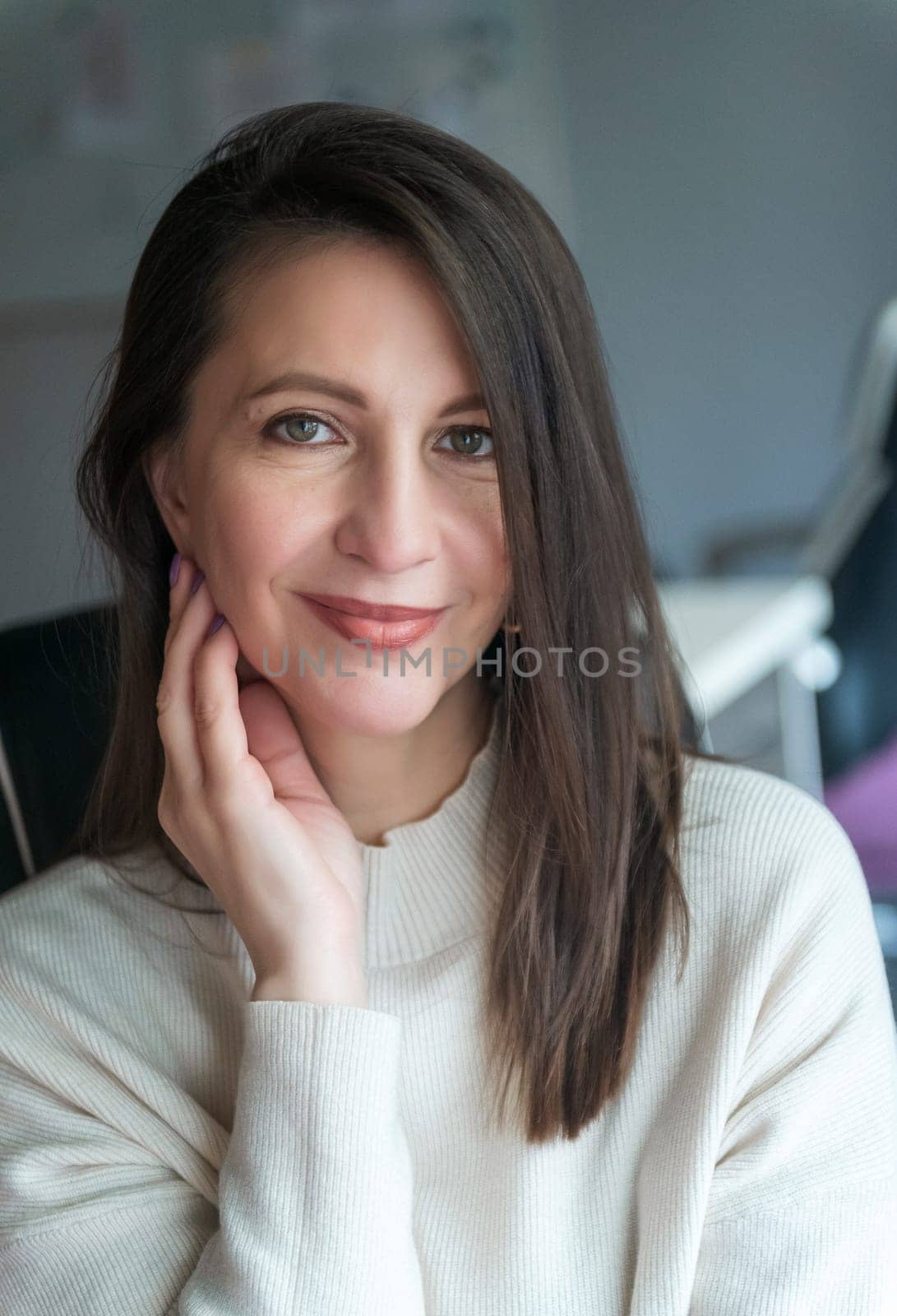 elegant woman over 40, business lady, works in the office. she is well-groomed, dressed in a white sweater. she smiles