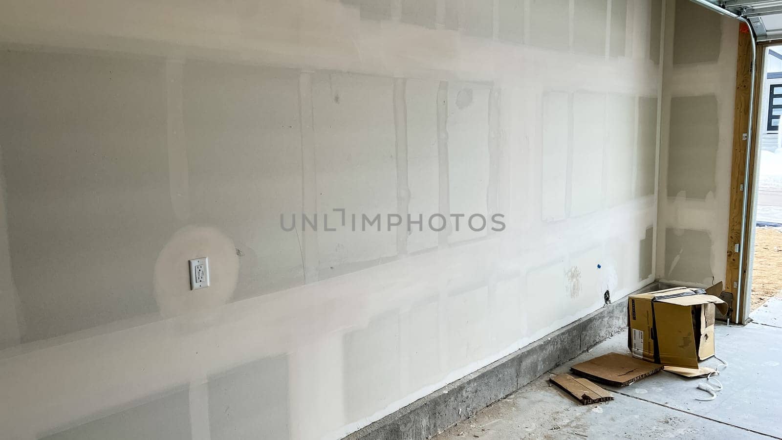 Castle Pines, Colorado USA - January 18, 2023-View of an unfinished garage interior in a single-family home under construction. Features drywall installation in progress, concrete flooring, and a cardboard box on the ground. The open garage door reveals a glimpse of the driveway and suburban neighborhood.