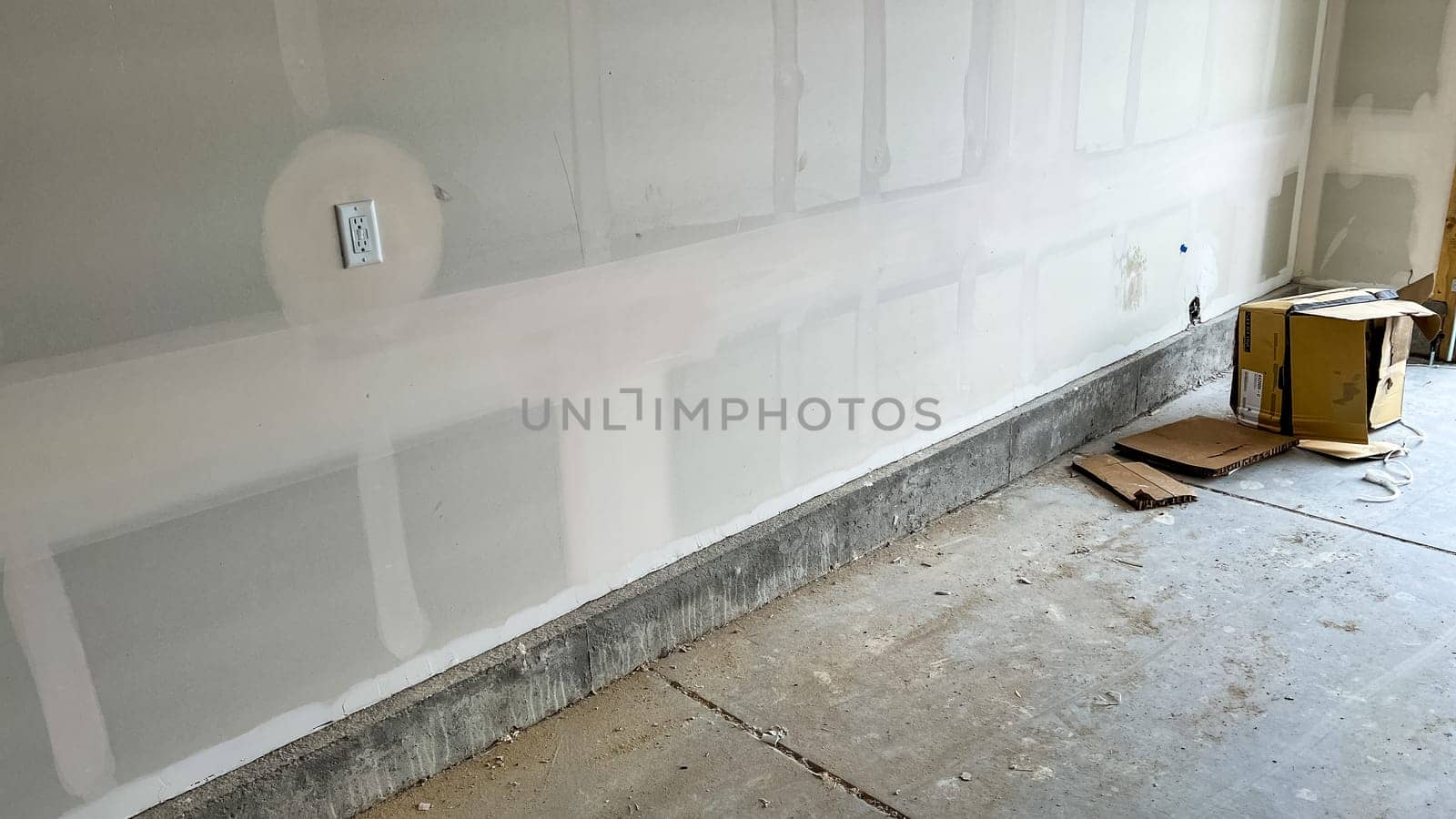 Castle Pines, Colorado USA - January 18, 2023-View of an unfinished garage interior in a single-family home under construction. Features drywall installation in progress, concrete flooring, and a cardboard box on the ground. The open garage door reveals a glimpse of the driveway and suburban neighborhood.