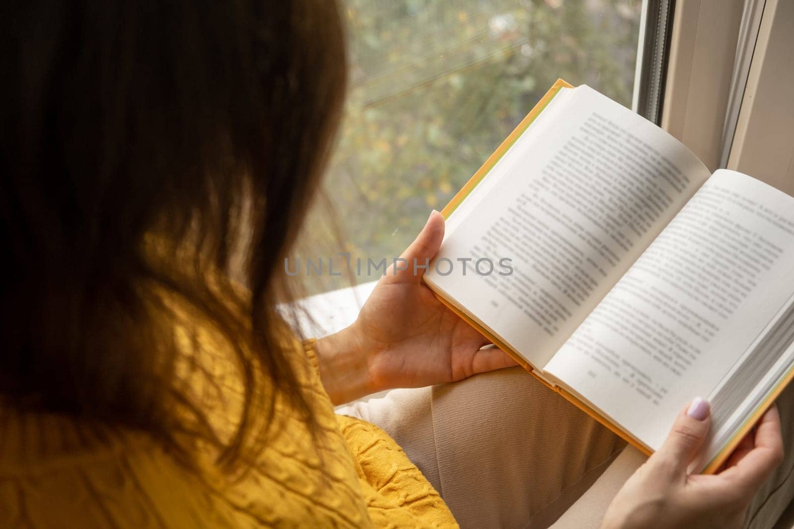 Young beautiful woman near window yellow knitted sweater read book by AnatoliiFoto