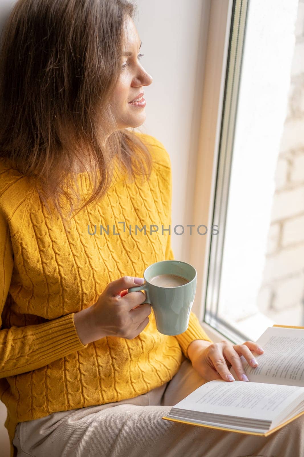 Young beautiful woman near window yellow knitted sweater read book by AnatoliiFoto