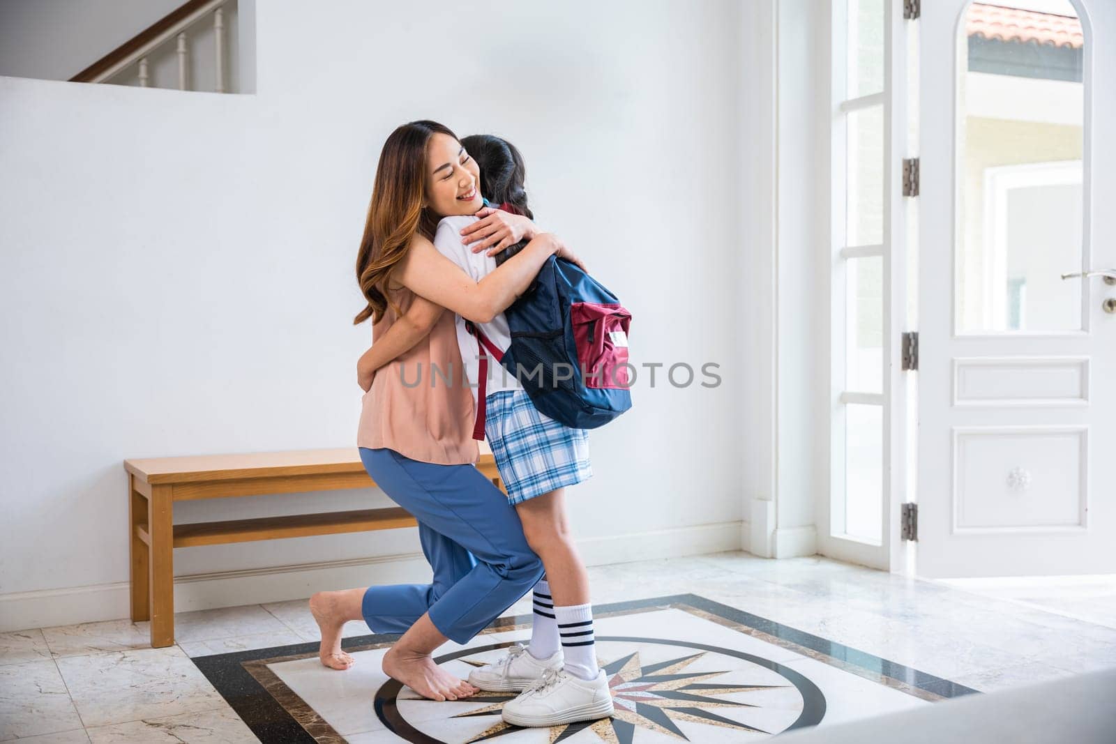 Asian mother hugging her daughter saying goodbye before go to school at home, loving mom and schoolgirl with backpack before first day, parents and child little girl