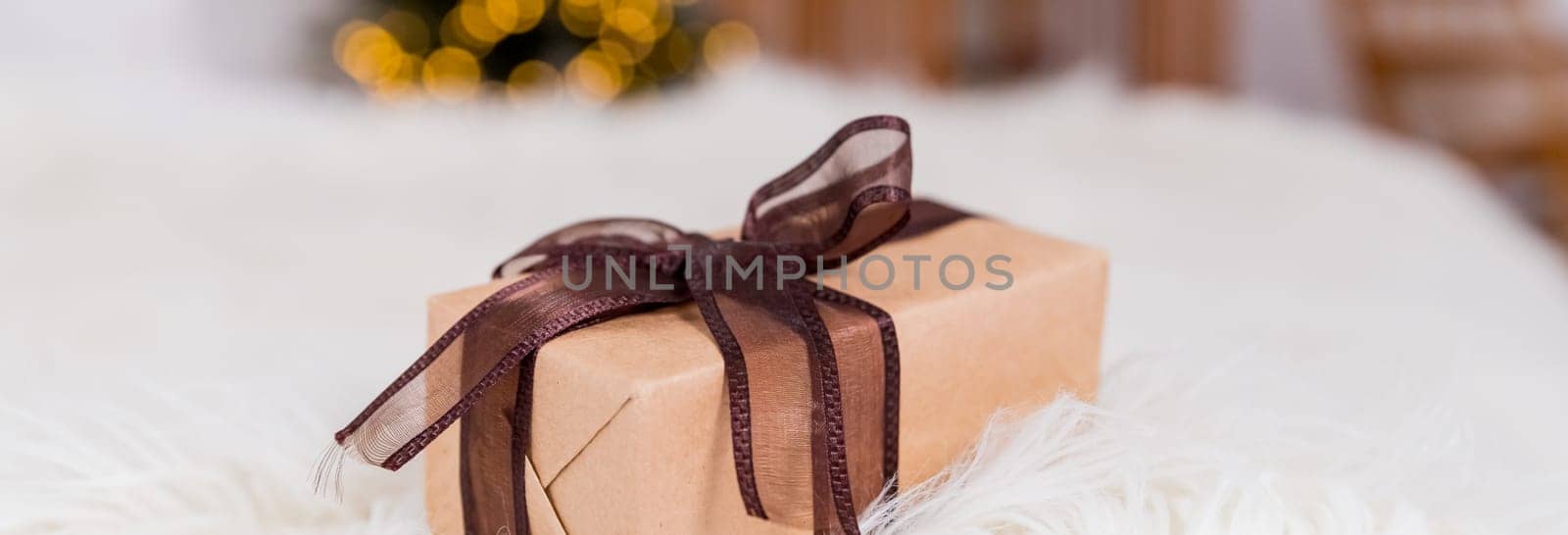 Wrapped Christmas presents on cozy bed next to Christmas tree with beautiful blurred lights on the background.