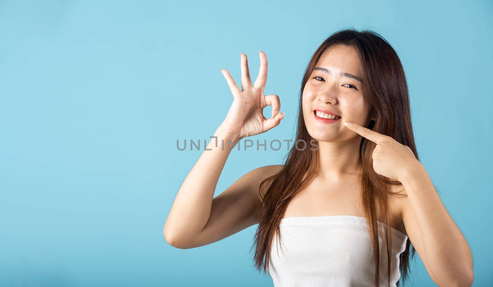 Beautiful female point fingers to smiling mouth and showing OK sign for good by Sorapop
