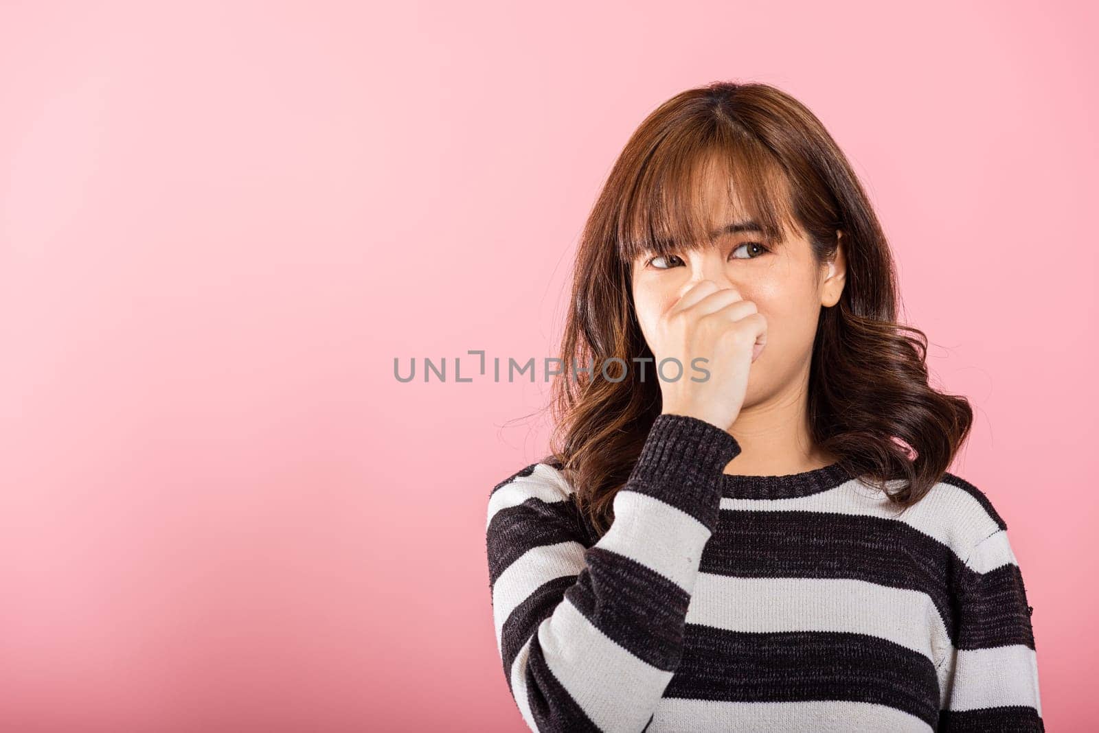 An unhappy Asian woman reacts to a foul smell by squeezing her nose by Sorapop