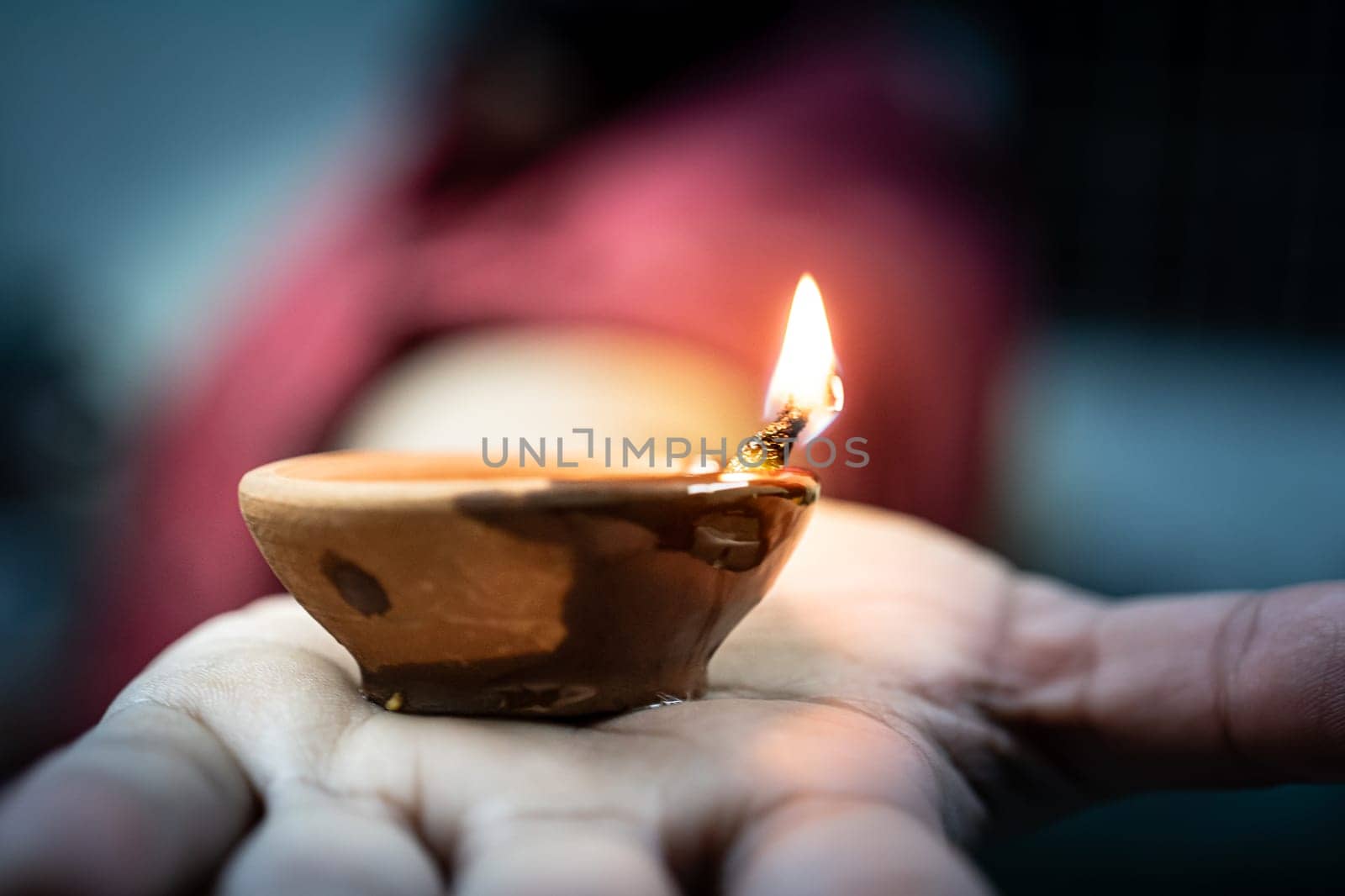 woman man holding out diya clay lamp with cotton wick soaked in oil burning, typical decoration during hindu festival diwali by Shalinimathur