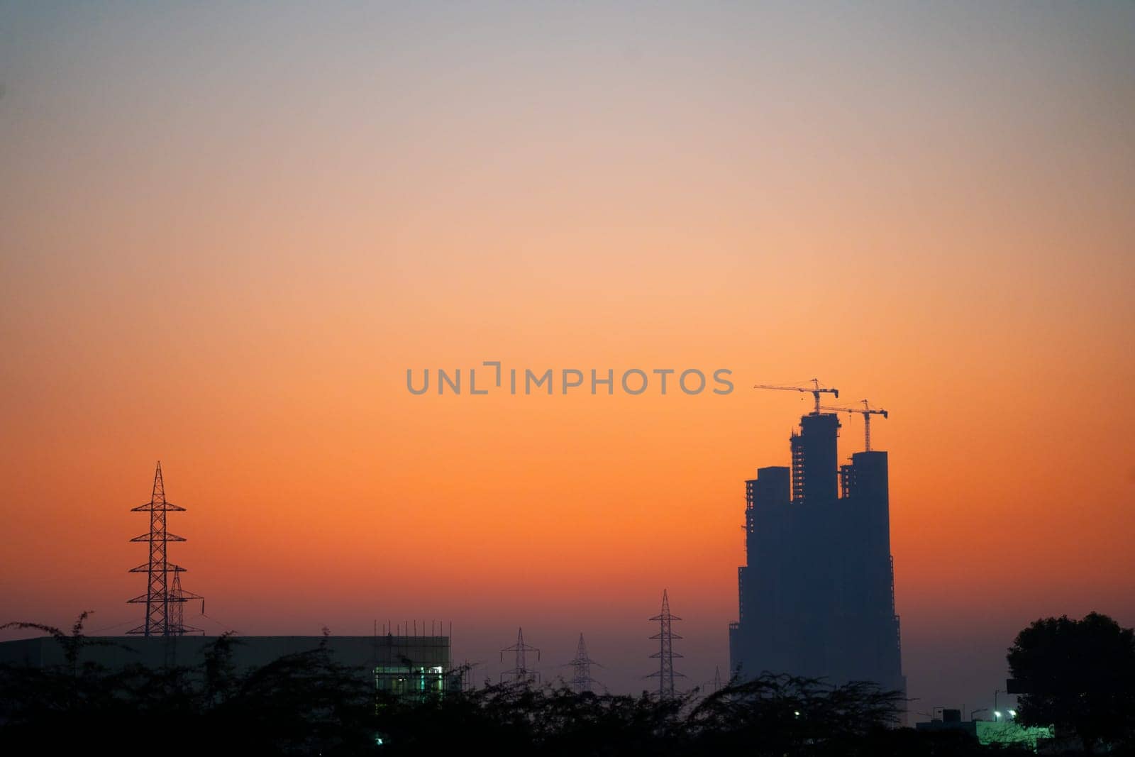 Evening dusk twilight shot showing under construction skyscraper multi story building silhouette against golden, red sky in Indian cities