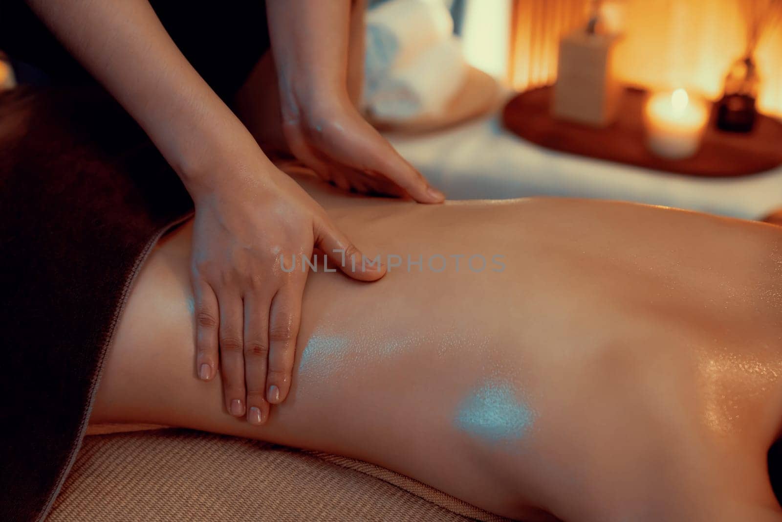 Closeup woman customer enjoying relaxing anti-stress spa massage and pampering with beauty skin recreation leisure in warm candle lighting ambient salon spa at luxury resort or hotel. Quiescent