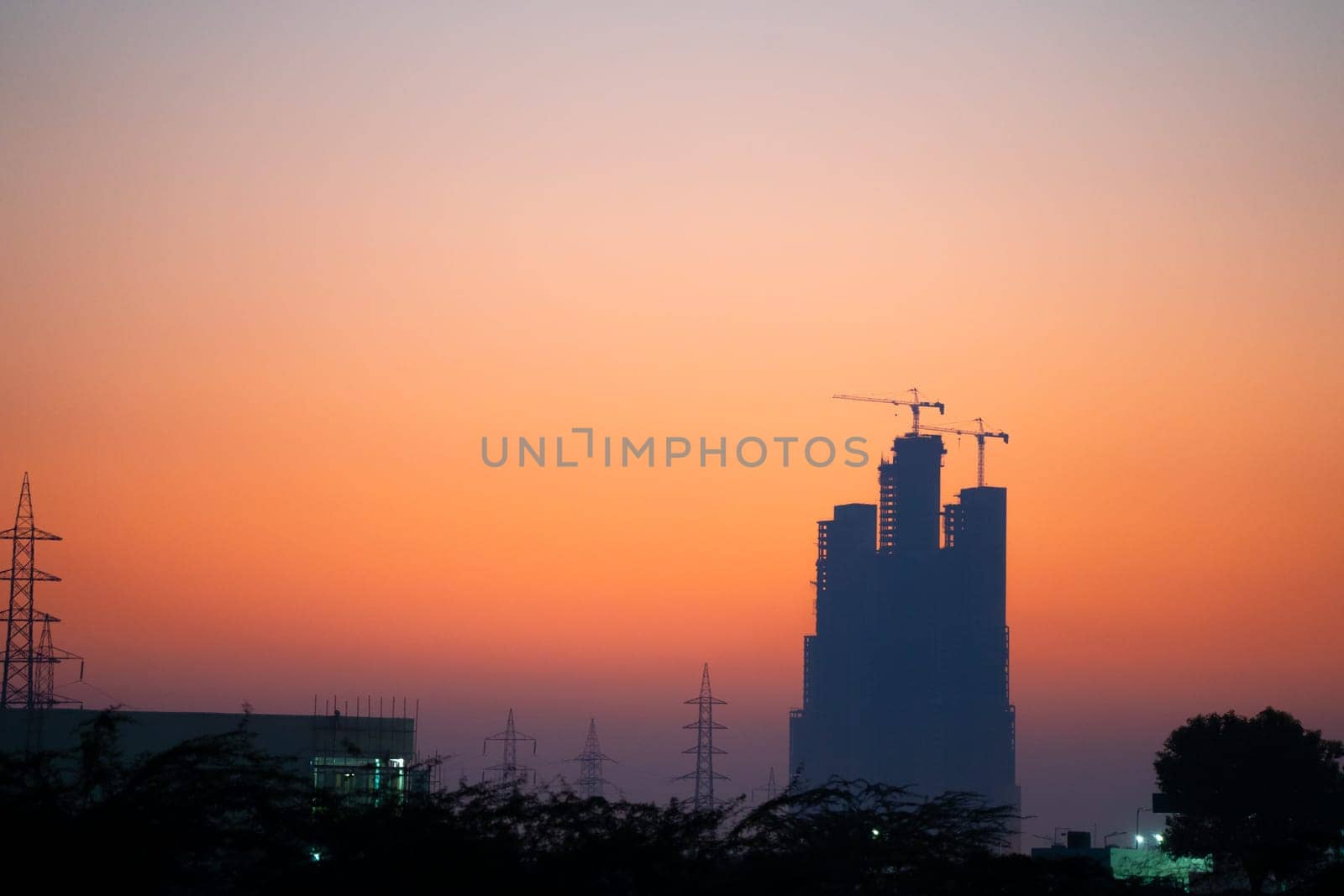 Evening dusk twilight shot showing under construction skyscraper multi story building silhouette against golden, red sky in Indian cities