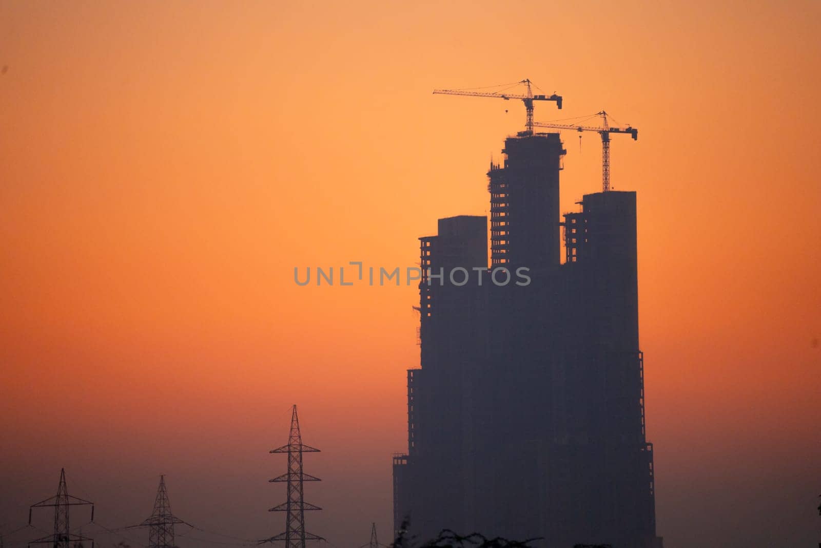 Evening dusk twilight shot showing under construction skyscraper multi story building silhouette against golden, red sky by Shalinimathur