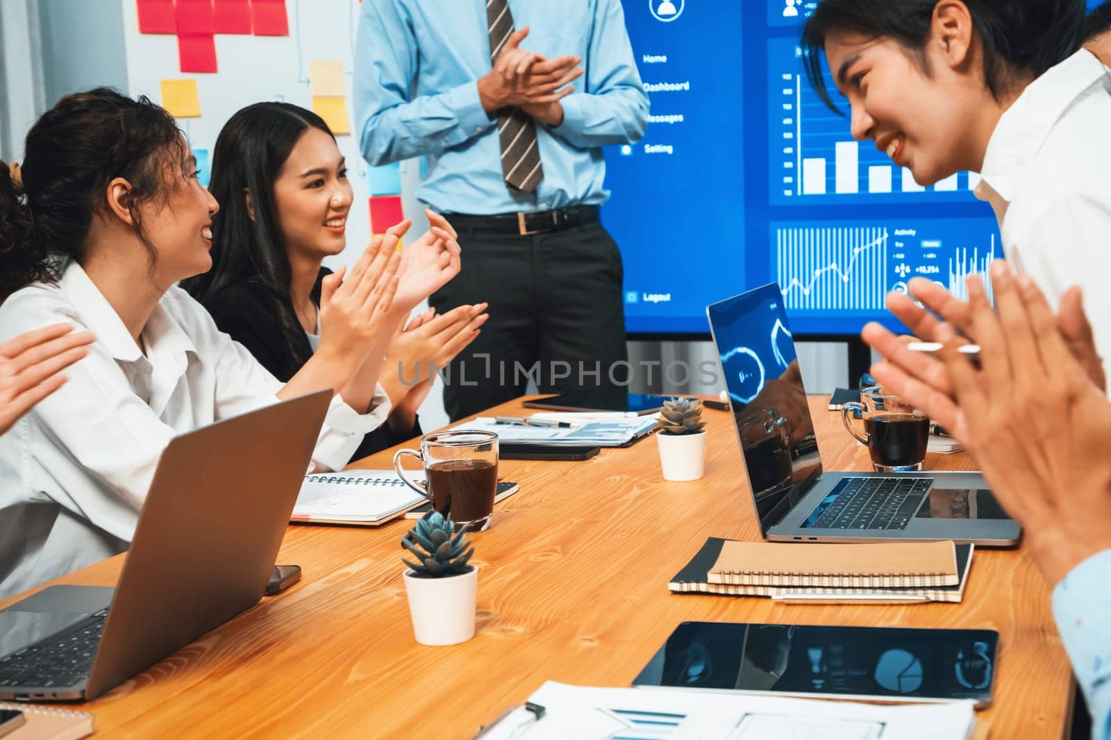 Group of happy multi ethnic businesspeople in celebratory gesture and successful teamwork after made success sales or positive financial data dashboard display on screen in meeting room. Habiliment