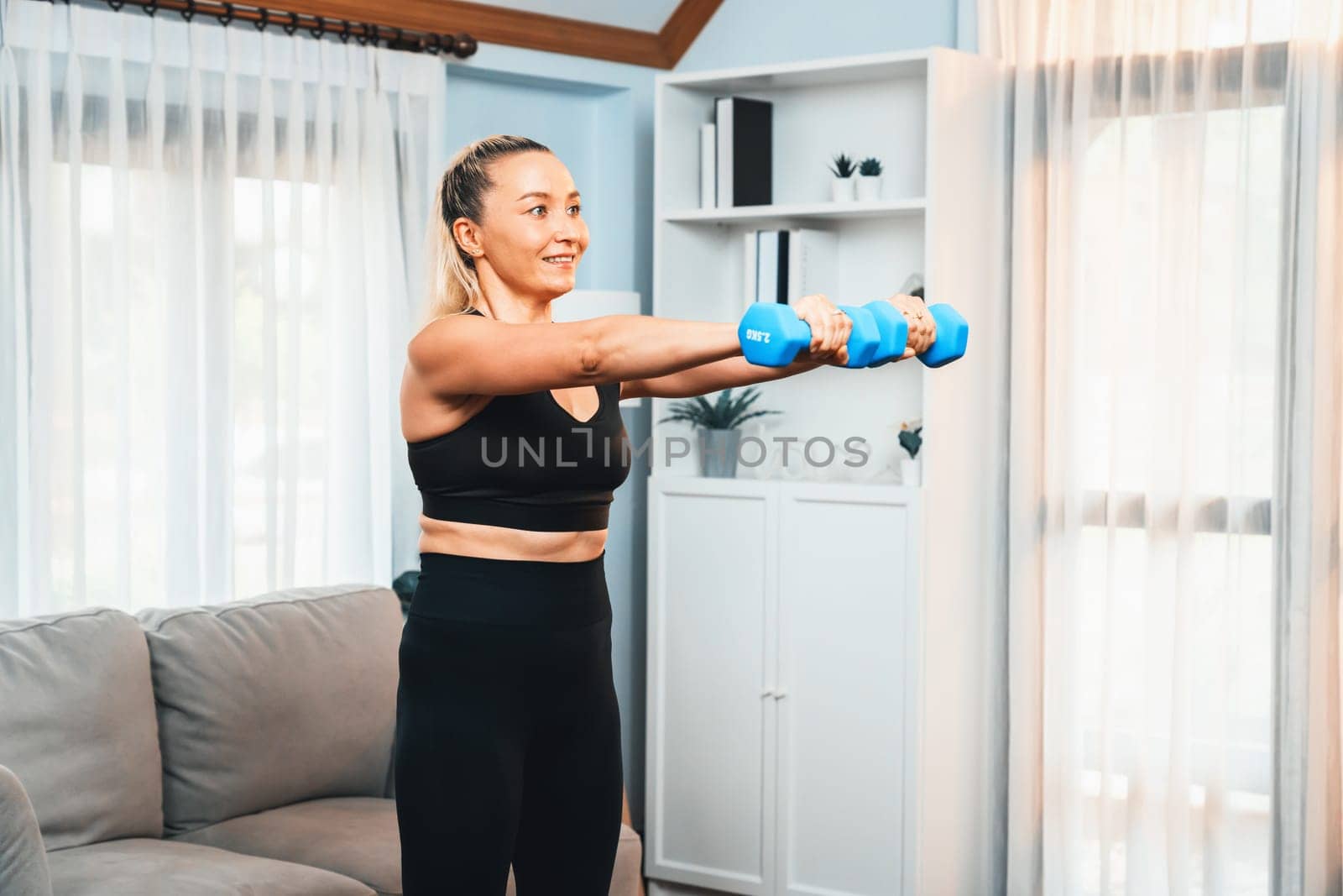 Athletic and sporty senior woman lifting dumbbell at home. Clout by biancoblue