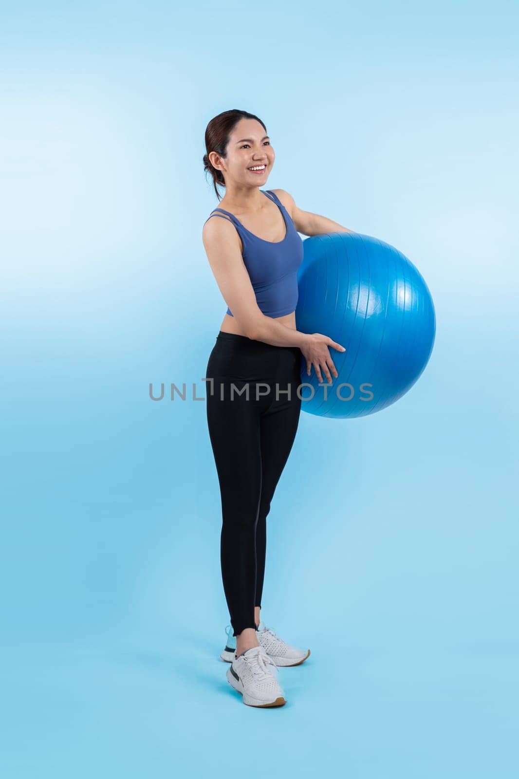 Young attractive asian woman portrait in sportswear with fit ball targeting on abs muscle for effective energetic daily workout routine. Studio shot and isolated background. Vigorous