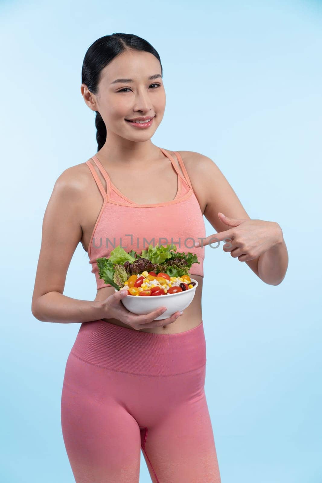 Young sporty Asian woman in sportswear holding salad bowl fill with vibrant of fruit and vegetable. Natural youthful and fit body lifestyle with balance nutrition on isolated background. Vigorous