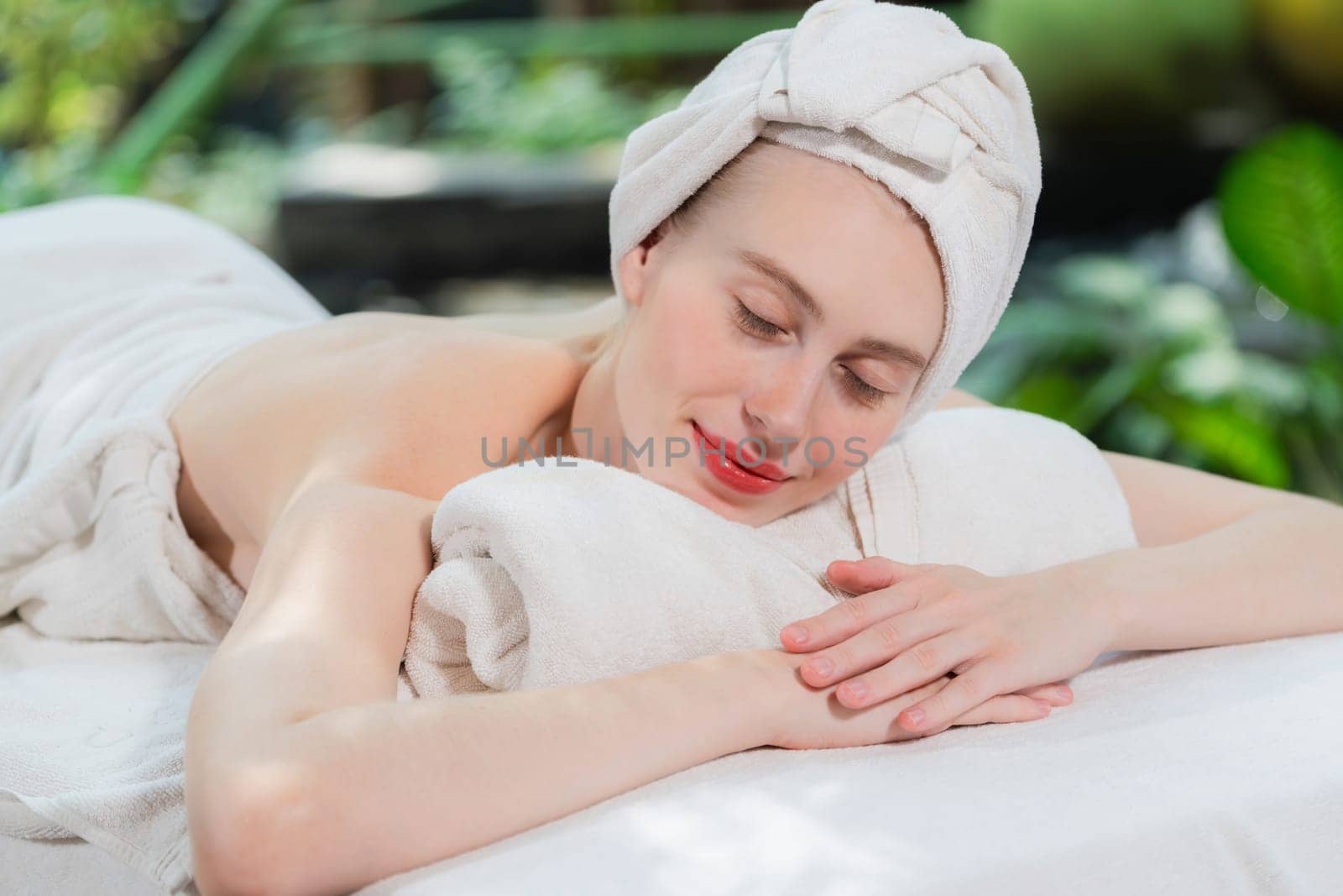 Beautiful young woman relaxes on a spa bed surrounded by nature. ready for a body massage. Attractive female in white towel lying peacefully during waiting for body massage. Close up. Tranquility