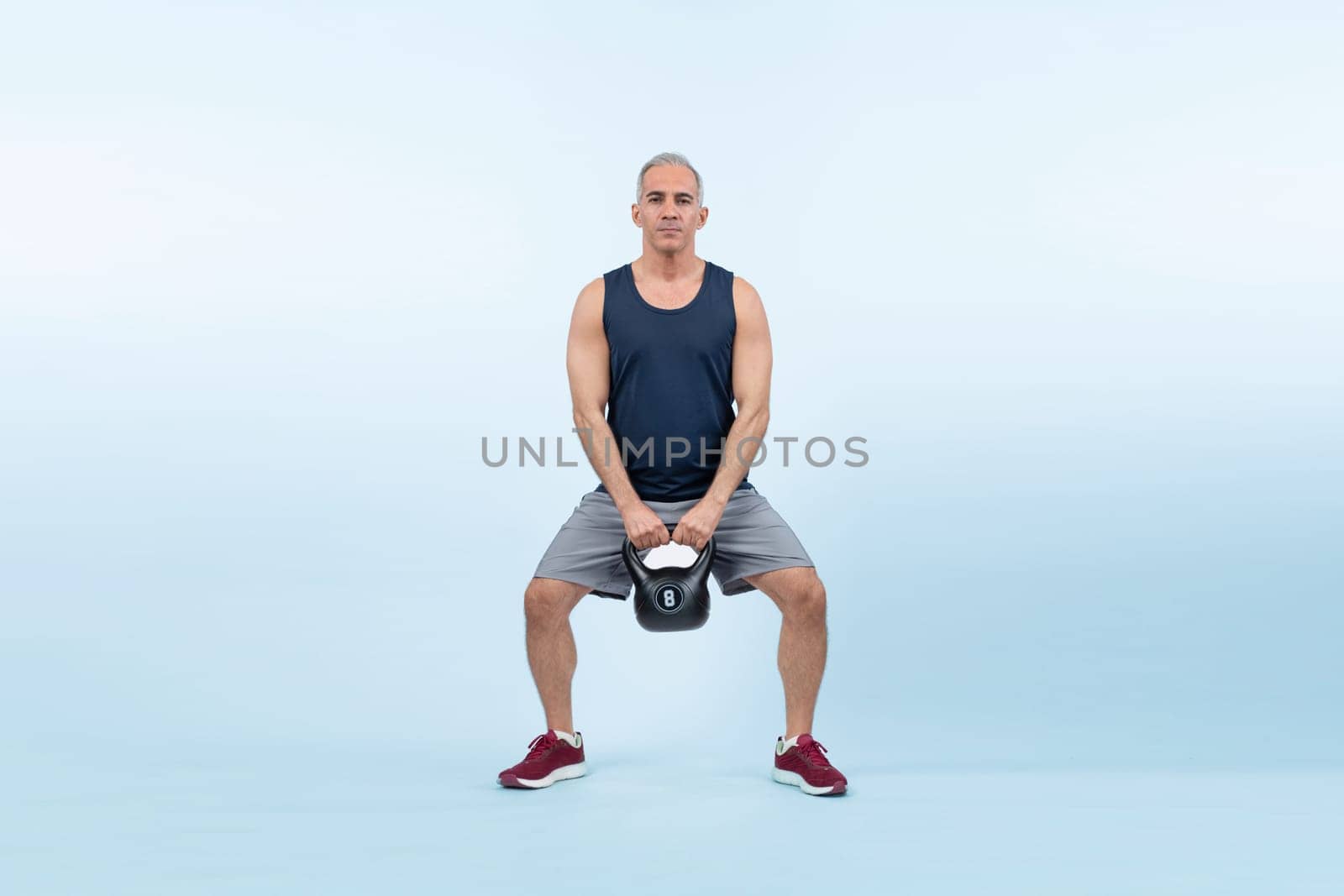Full body length shot athletic senior man doing squat with weight. Clout by biancoblue