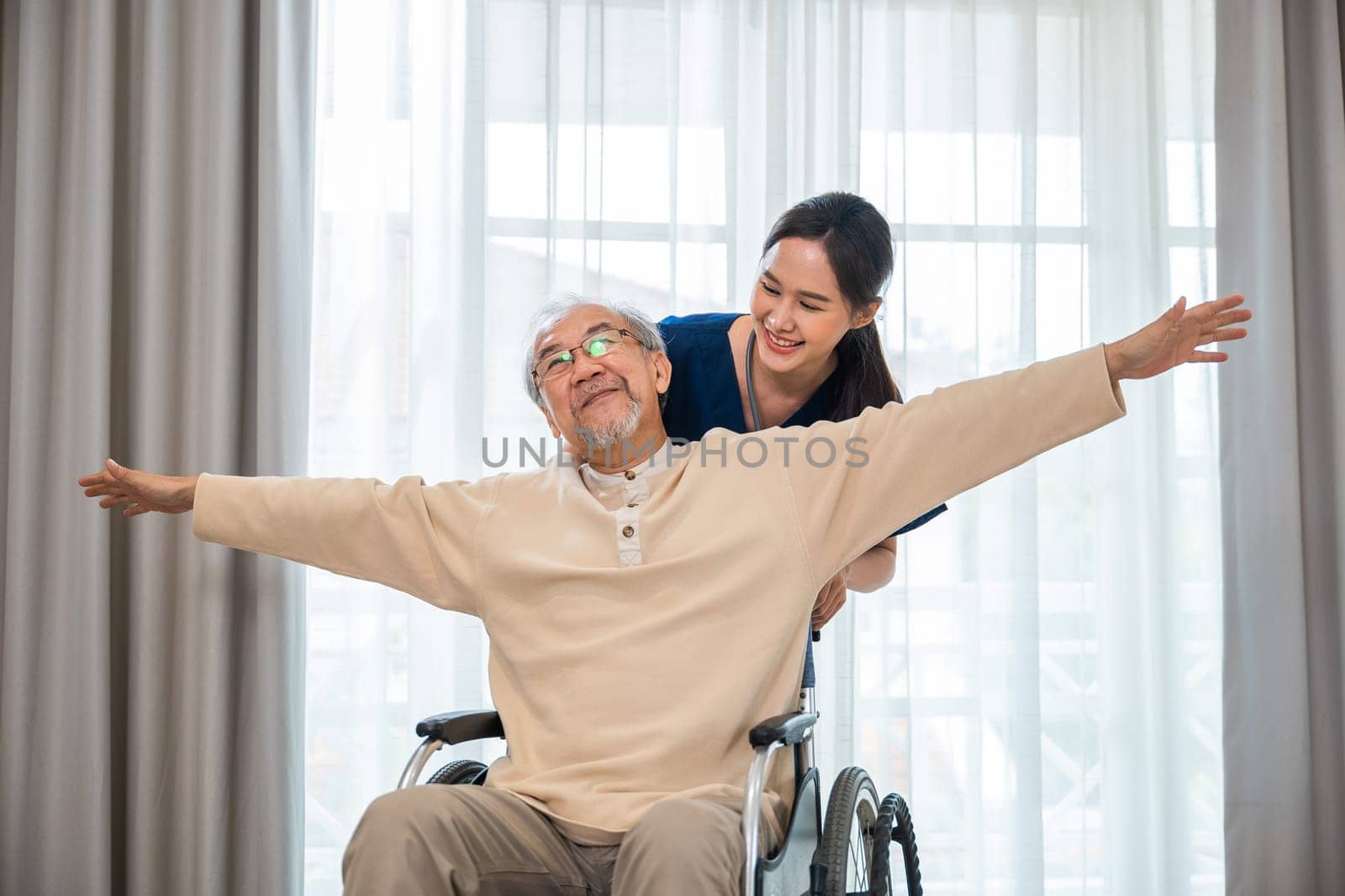 Happy curator person doctor pushing and walk elderly patient freedom raising arm at hospital, Asian senior retired old man sitting on wheelchair having fun with young woman nurse, disabled sanatorium