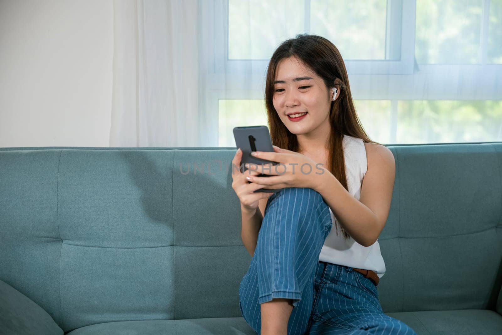 Happy beautiful woman relaxation she shopping online with smartphone, Smiling Asian female sitting on sofa talking mobile smart phone at living room at home, Social media networks communication