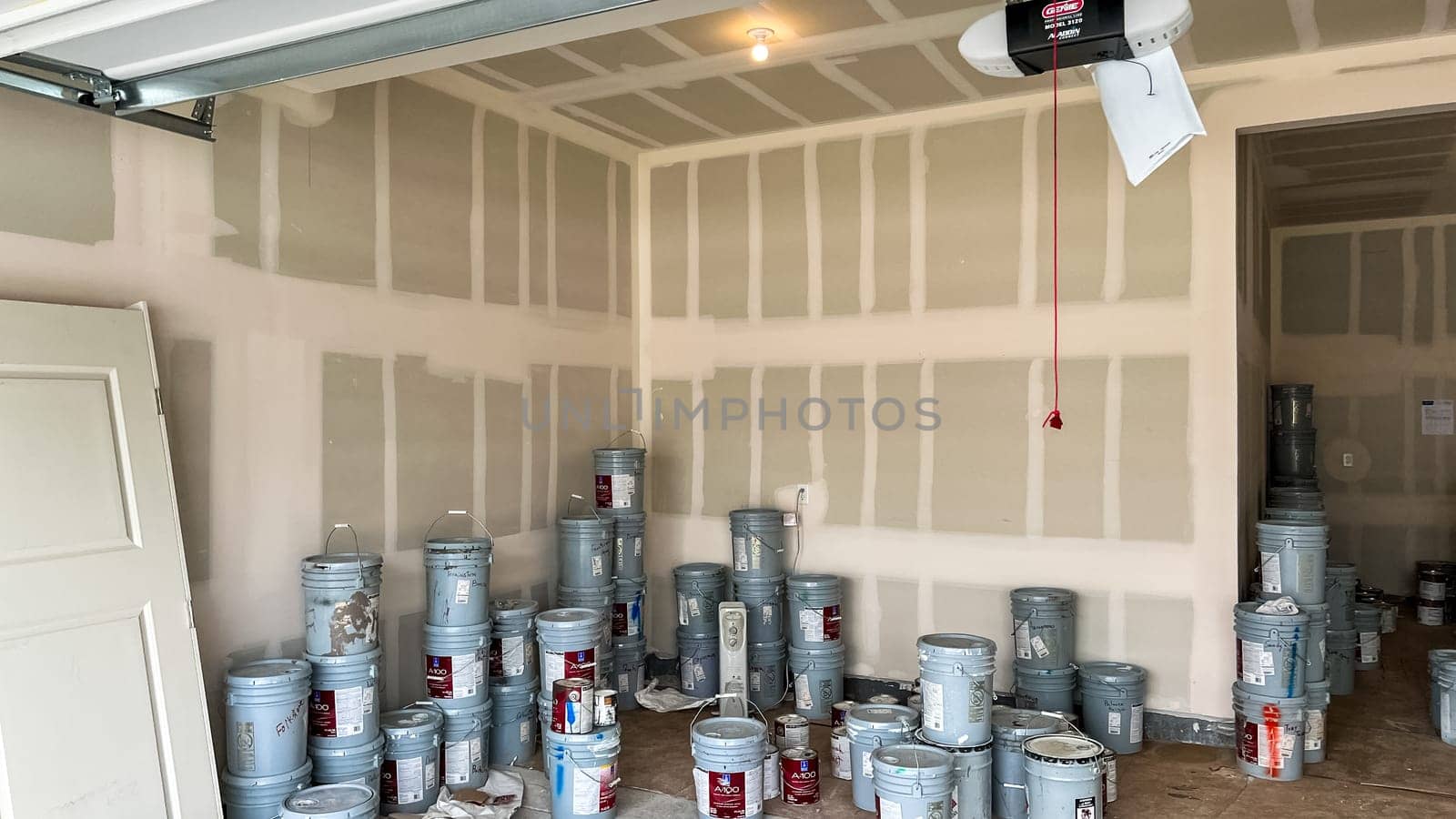 Castle Pines, Colorado USA - January 18, 2023-Garage interior of a new single-family home under construction, featuring numerous paint buckets stacked on the concrete floor. Unfinished drywall lines the walls, and the scene highlights the materials used during the home-building process.