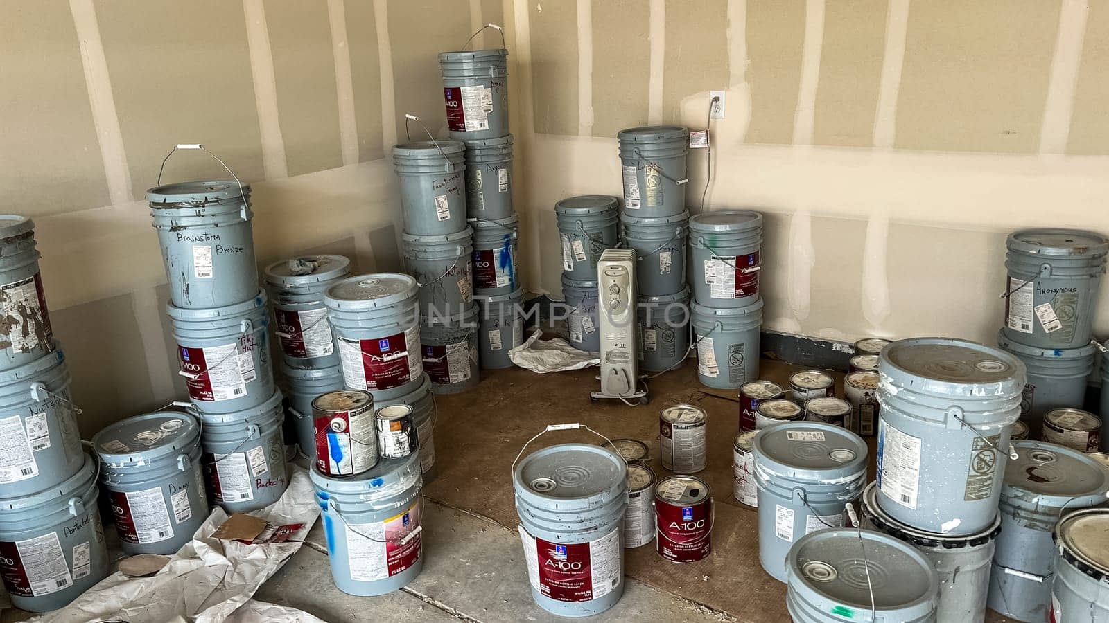 Castle Pines, Colorado USA - January 18, 2023-Garage interior of a new single-family home under construction, featuring numerous paint buckets stacked on the concrete floor. Unfinished drywall lines the walls, and the scene highlights the materials used during the home-building process.