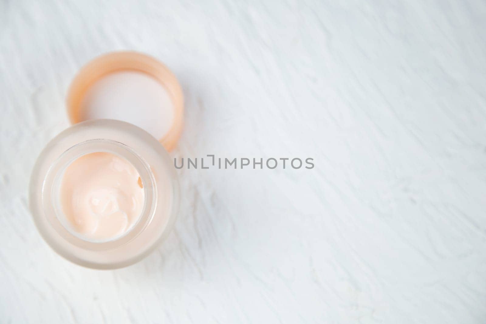 Cream of delicate peach color in a glass jar on a white textured background. High quality photo