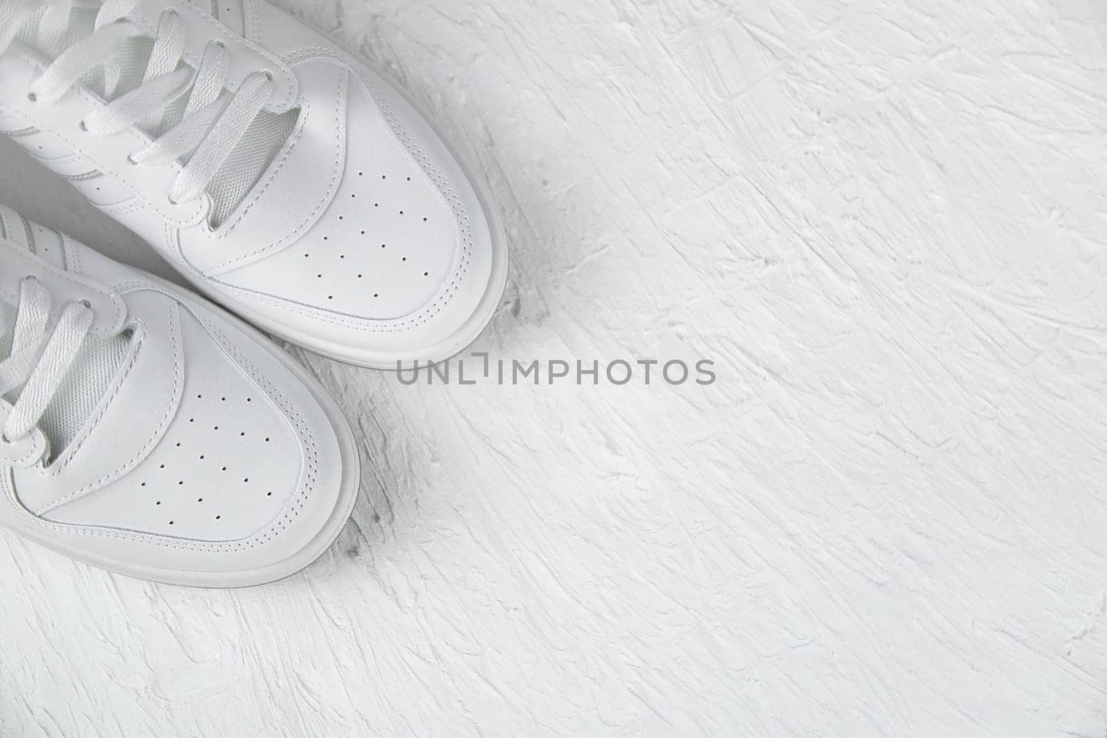 White leather sneakers stand in the left corner on a white textured background. High quality photo