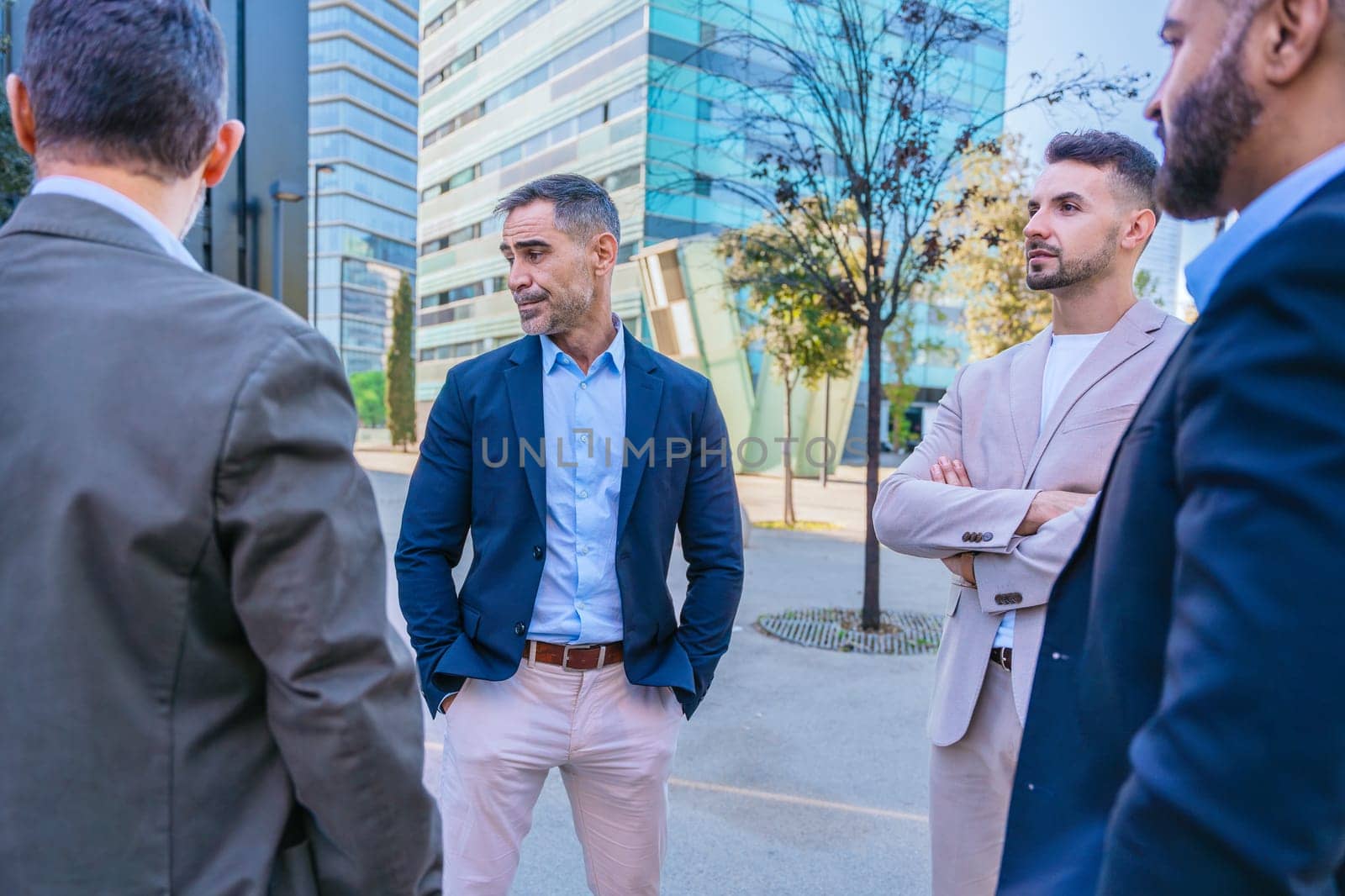 A group of business professionals engaged in a serious discussion outdoors. They are dressed in formal and smart casual attire, with a modern cityscape in the background.