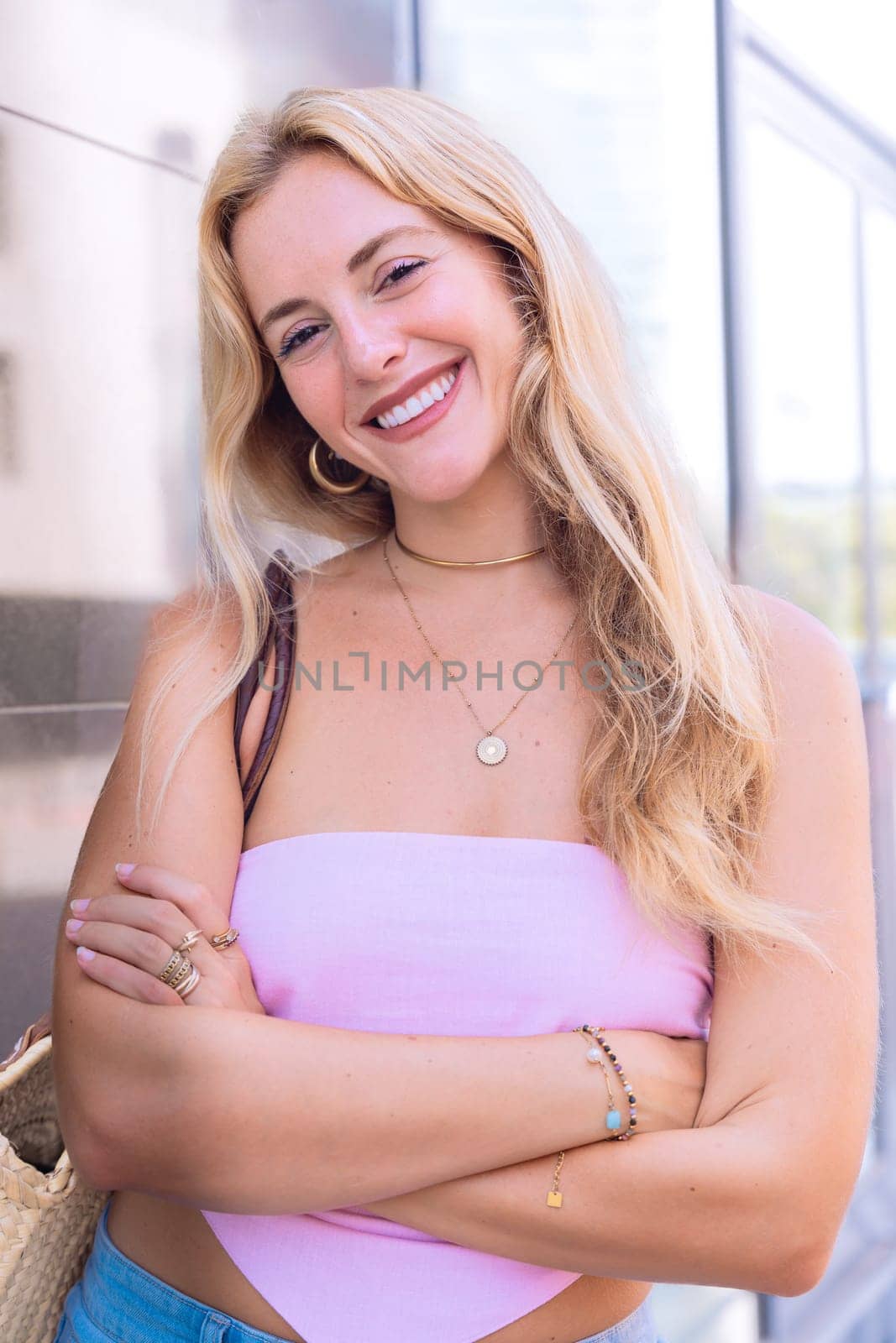 A blonde woman standing confidently with arms crossed, wearing a trendy summer outfit. Captured in an urban setting with a casual and fashionable vibe, showcasing modern elegance.