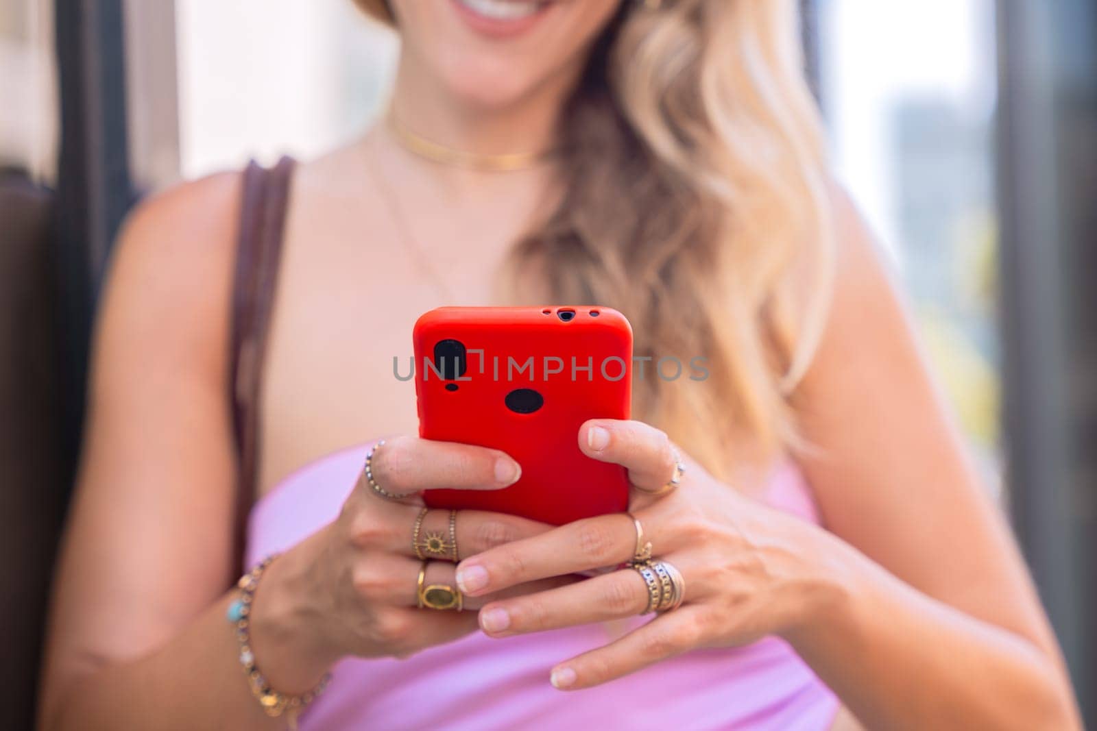 A blonde woman standing outdoors, focused on her smartphone. Captured in a modern urban environment, highlighting casual elegance, digital connectivity, and a relaxed lifestyle.
