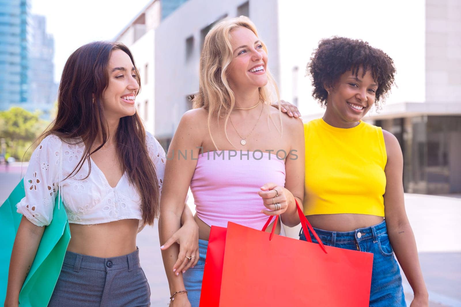 Three young women enjoying a sunny day, carrying shopping bags and smiling as they walk in an urban environment. Perfect for concepts like friendship, shopping, fashion, and lifestyle.
