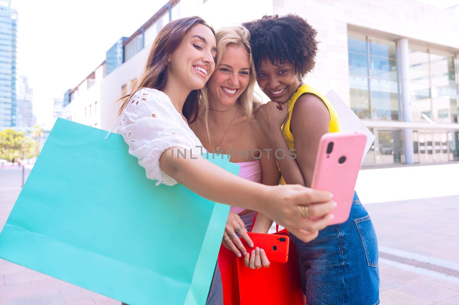 Three young women sitting outdoors, smiling, and taking a playful selfie together. Perfect for concepts like friendship, happiness, social media, and outdoor lifestyle.