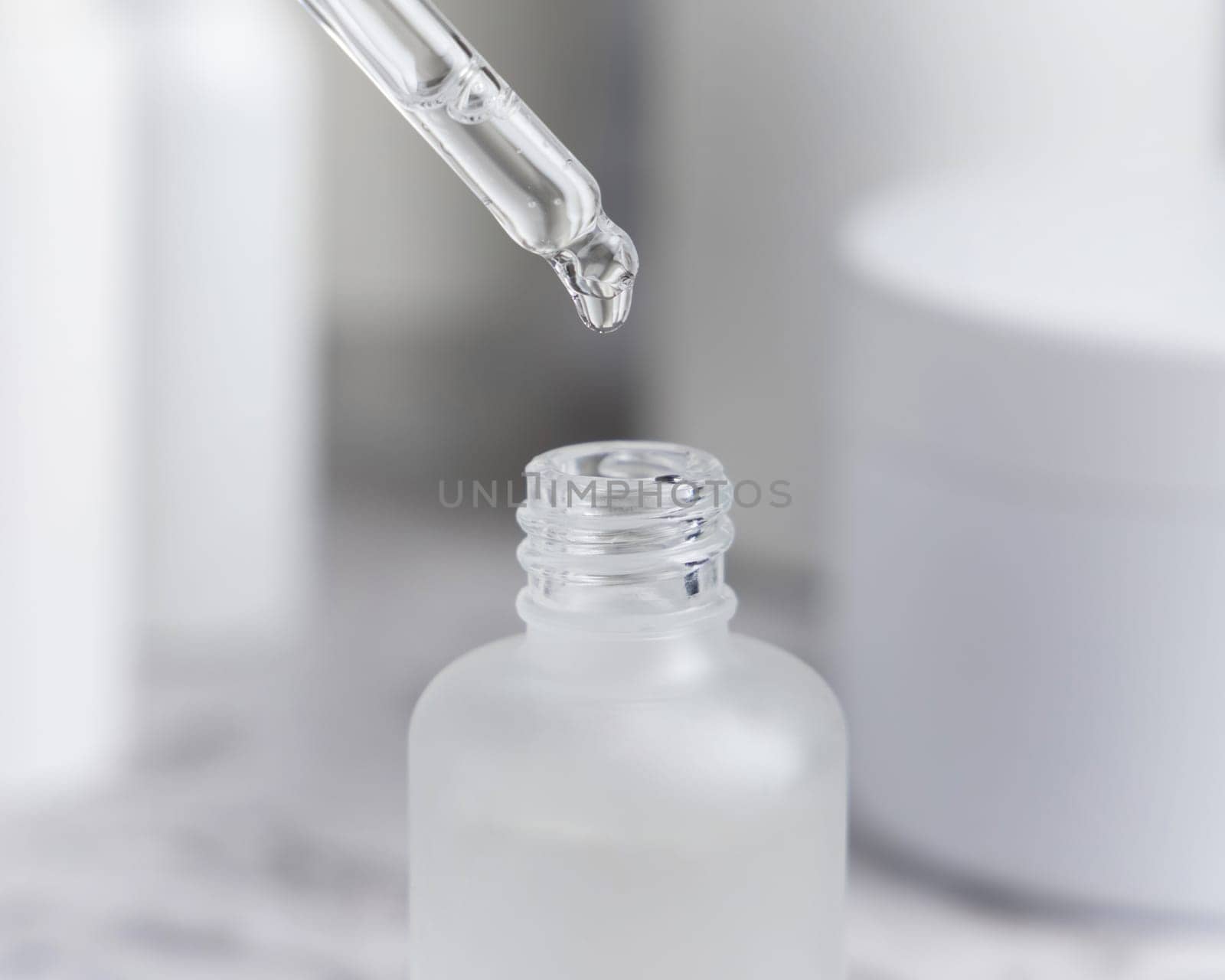 Drop falls from a pipette inside a trasparent glass dropper bottle against cosmetics in bathroom closeup. Natural organic serum or essence or for beauty routin, monochrome