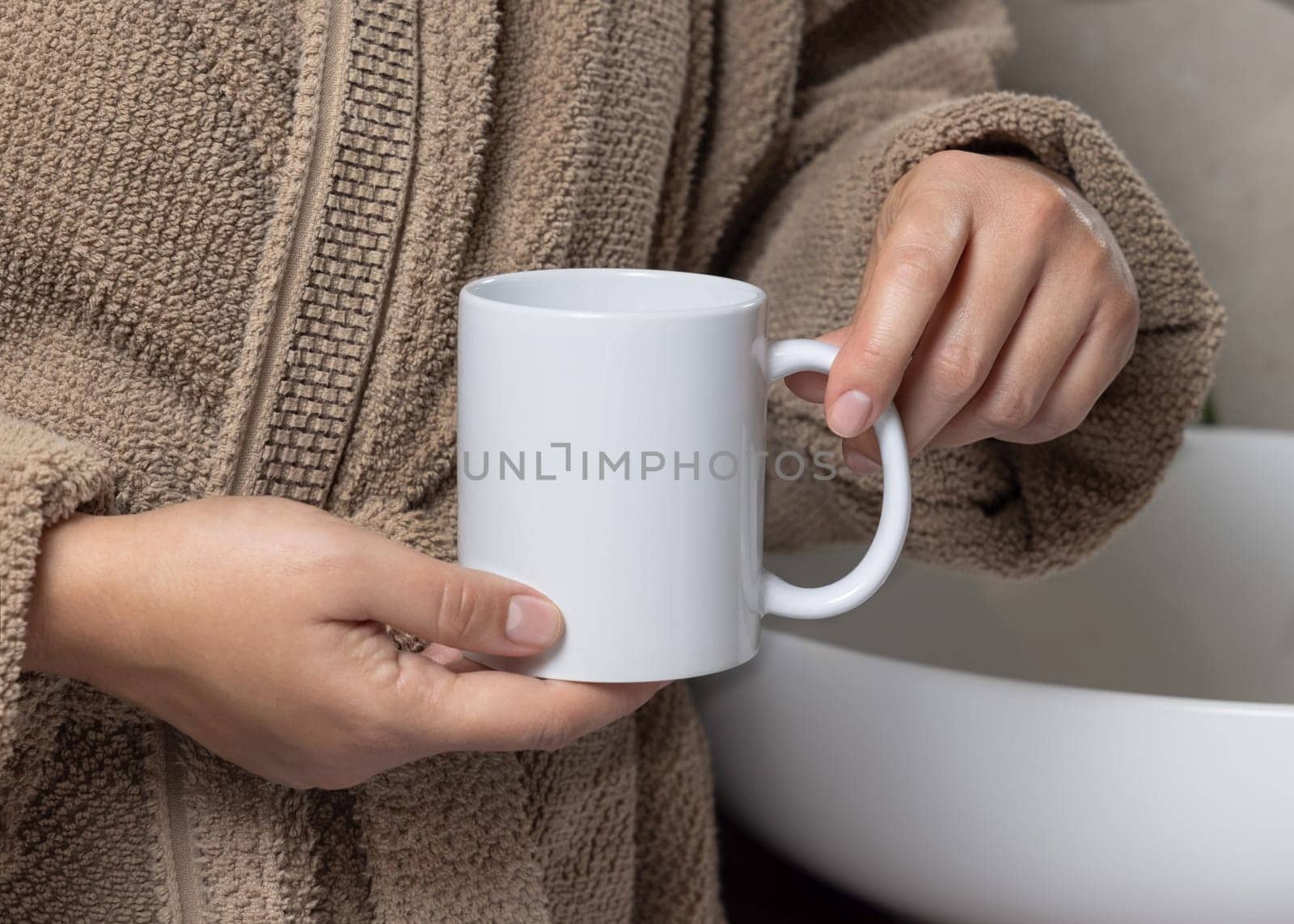Close up of woman in light brown bathrobe 11 oz white blank coffee mug in hands, mockup. Hands with natural manicure. Template for your design with copy space