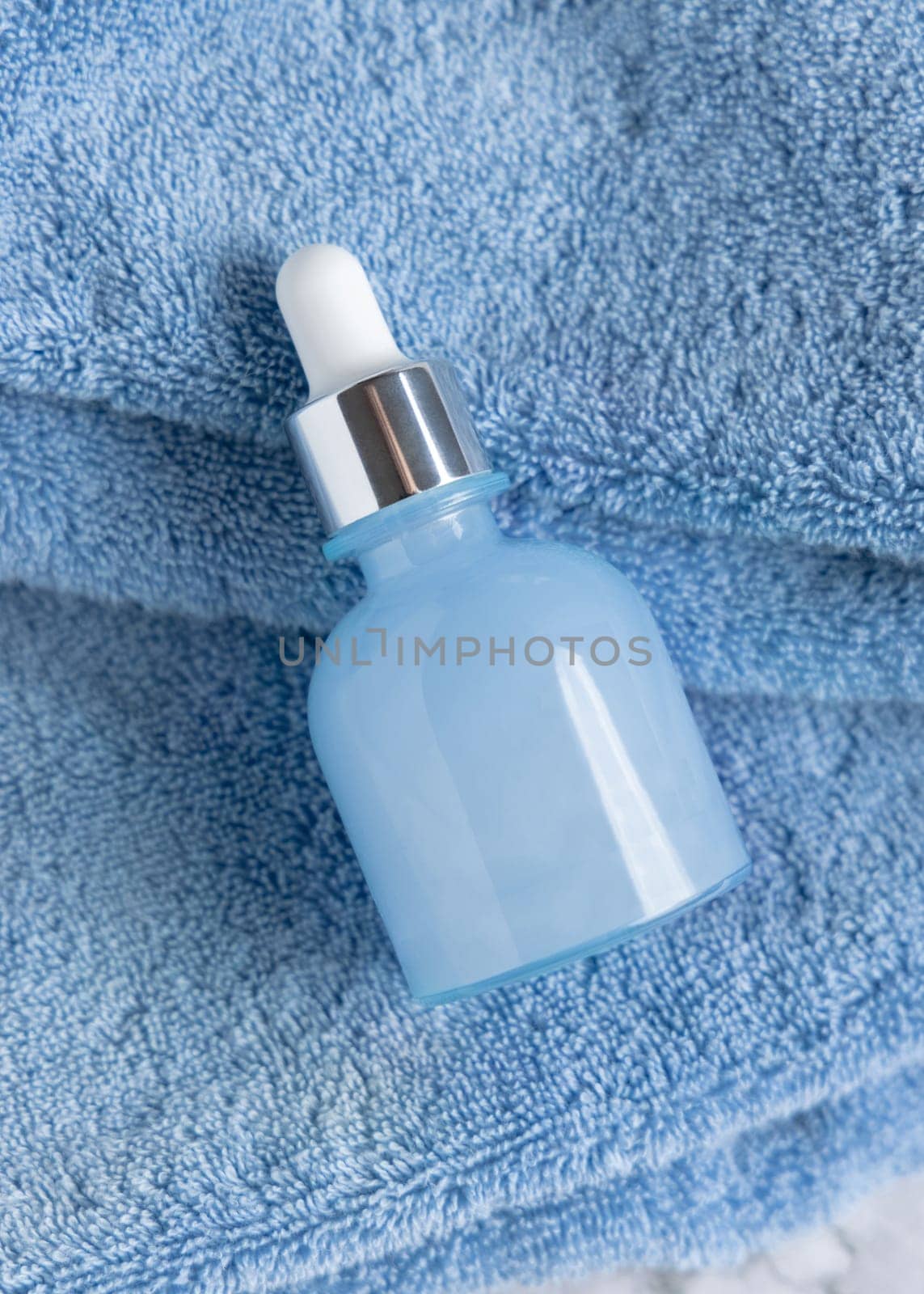 Light blue glass dropper bottle with copy space on blue towels top view, packaging mockup. Natural cosmetic product for facecare, Essence for Spa and Wellness