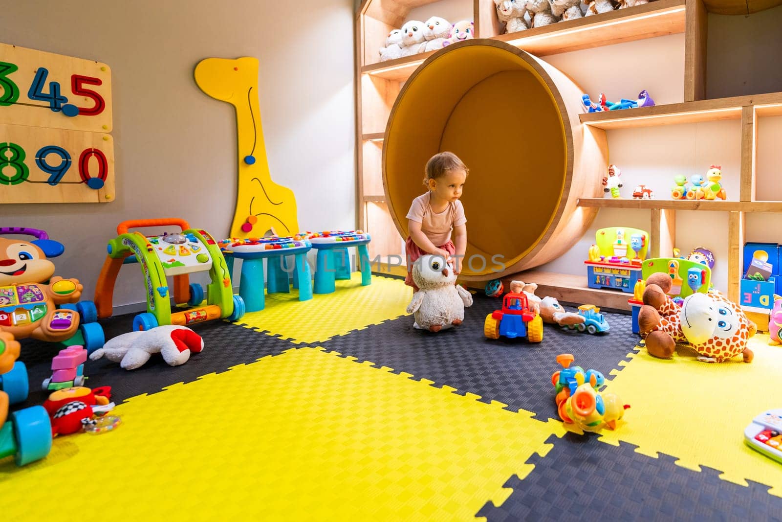 Toddler exploring colorful indoor playroom with plush toys, games, and educational activities