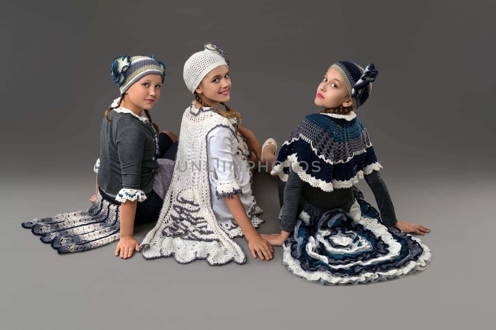 Pretty girls wearing fashion white and blue costumes and hats sitting on the floor rearview