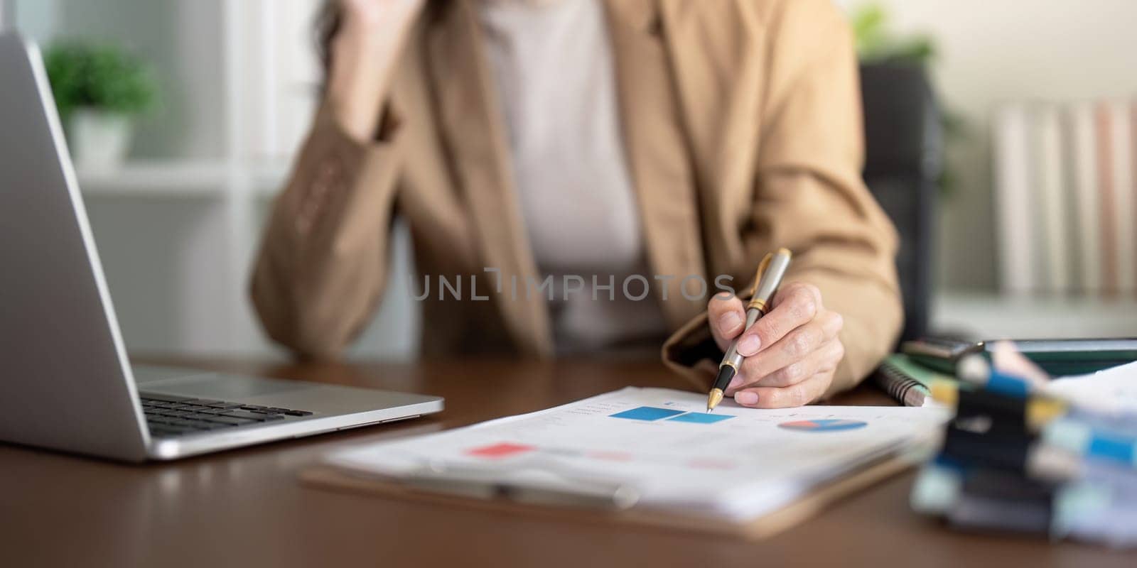 A businesswoman reviewing important financial data and charts on a clipboard at her modern office desk, showcasing analytical skills and concentration.