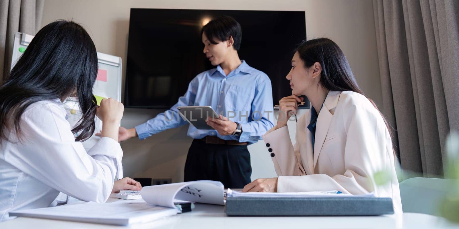 A focused team of professionals in a sleek office setting, engaging in a discussion led by a young man with a tablet, strategizing on a presentation.