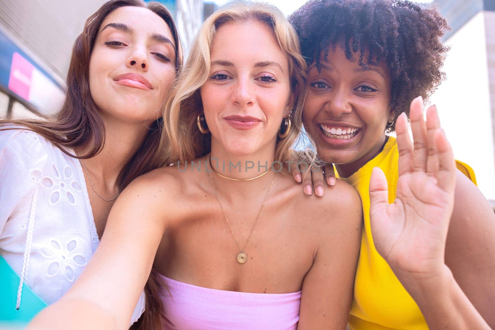 Three young women sitting outdoors, smiling, and taking a playful selfie together. Perfect for concepts like friendship, happiness, social media, and outdoor lifestyle.