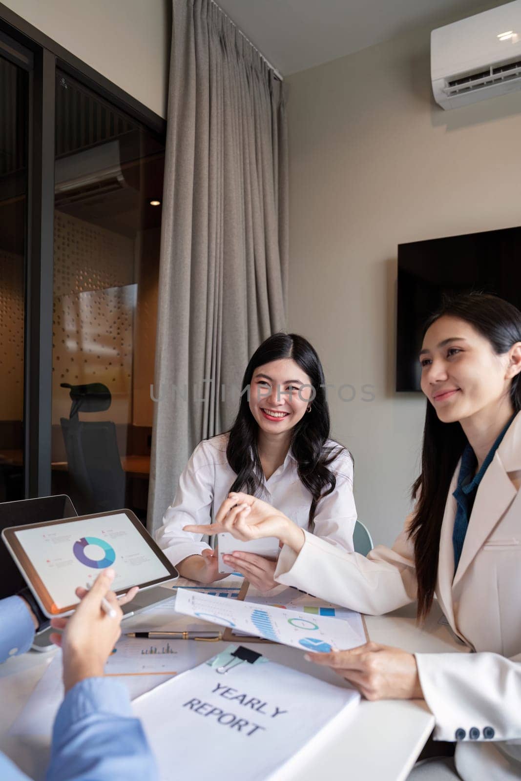 Two confident female professionals discussing and reviewing the yearly report using a digital tablet, while sharing insights in a modern office setting.