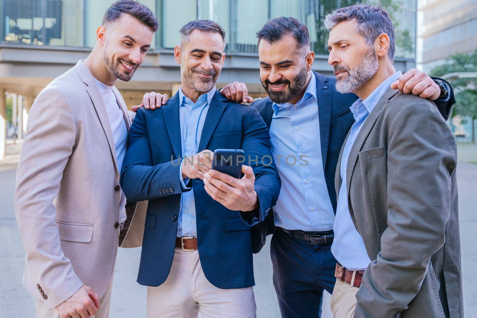 A group of confident businessmen standing outdoors in a modern urban setting. They are smiling and looking at a smartphone, symbolizing teamwork, technology, and connection.