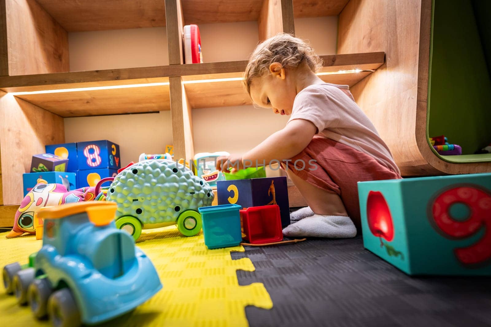 Toddler playing with colorful blocks and toys in a bright and interactive playroom