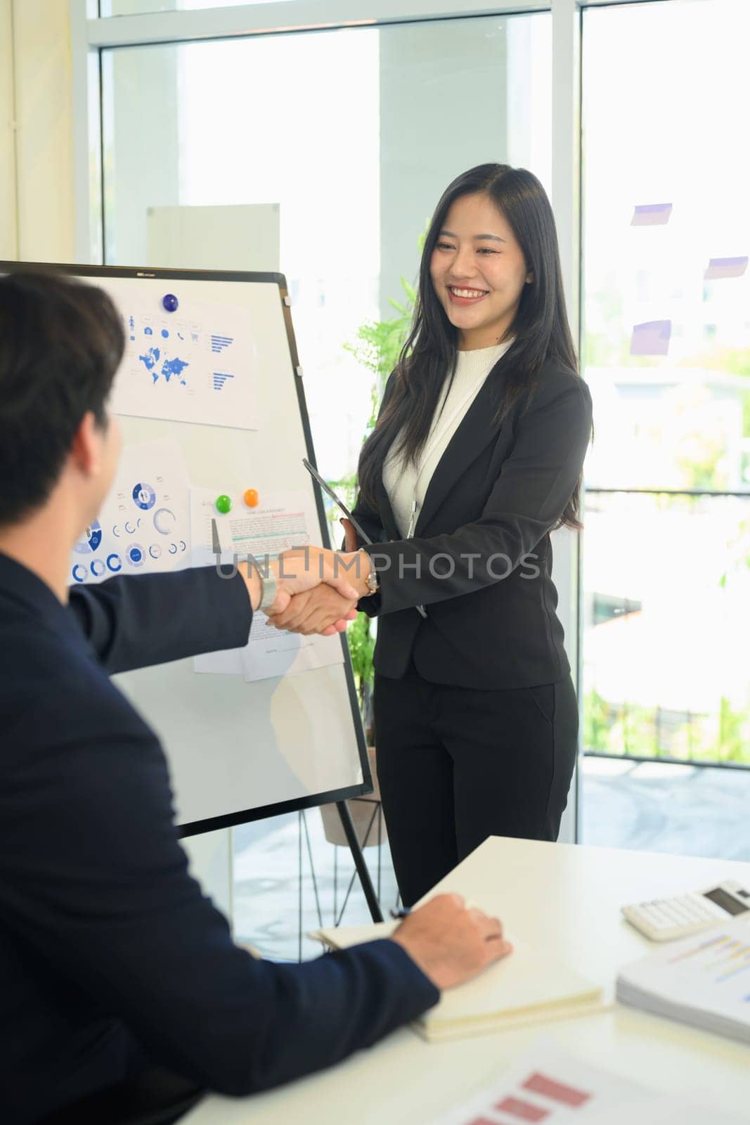 Confident businesswoman in formal suit shaking hands with colleague during meeting in modern office.