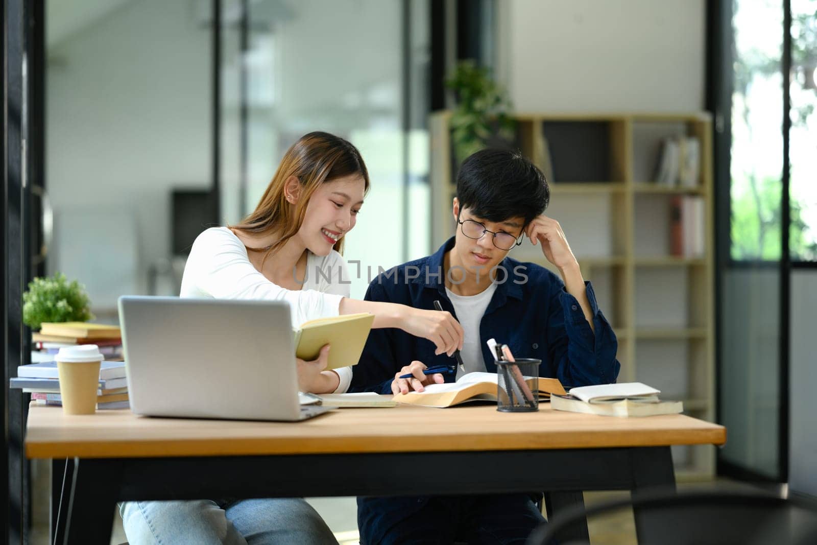 Two university students sharing ideas while studying together in a library. Education concept.