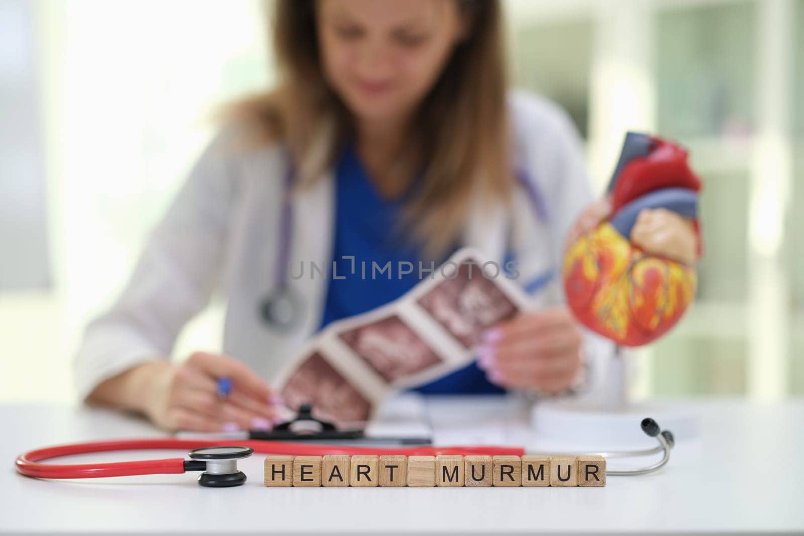 A qualified doctor examines heart images and models, focusing on diagnosing heart murmurs in a medical setting
